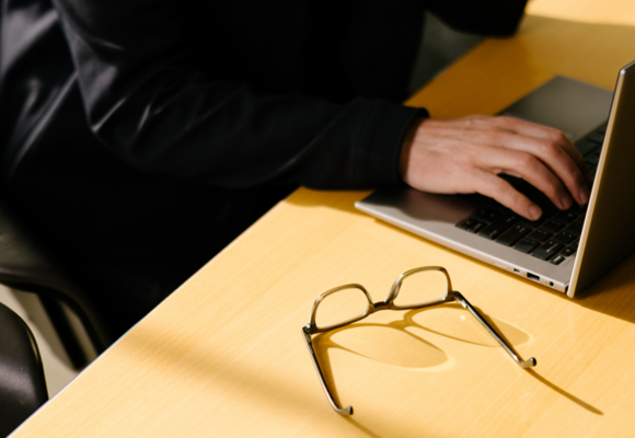 Personne à un bureau avec un ordinateur portable générant un rapport ESG du bâtiment, lunettes posées sur la table.